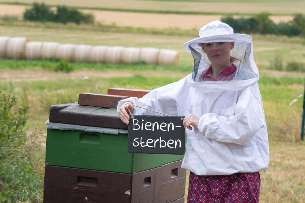 Imkerin hält Kreidetafel mit dem Wort Bienensterben hoch